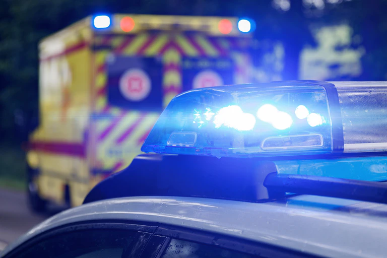 Ein gelber Rettungswagen steht im Hintergrund, im Vordergrund ist das Blaulicht eines Polizeiautos angeschnitten. — © Symbolbild